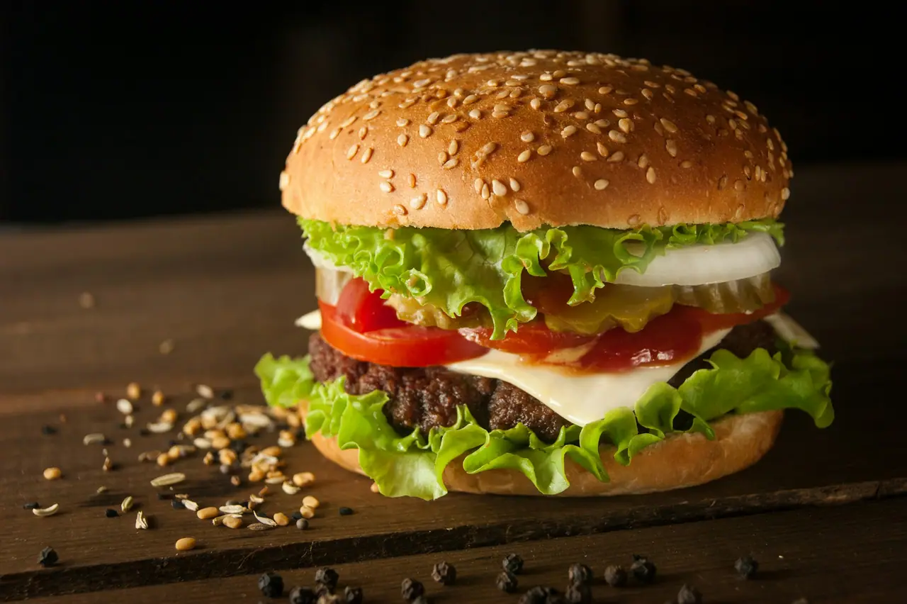 Hambúrguer Brasa Clássico com cheddar derretido, alface e tomate sobre tábua de madeira, em fundo escuro