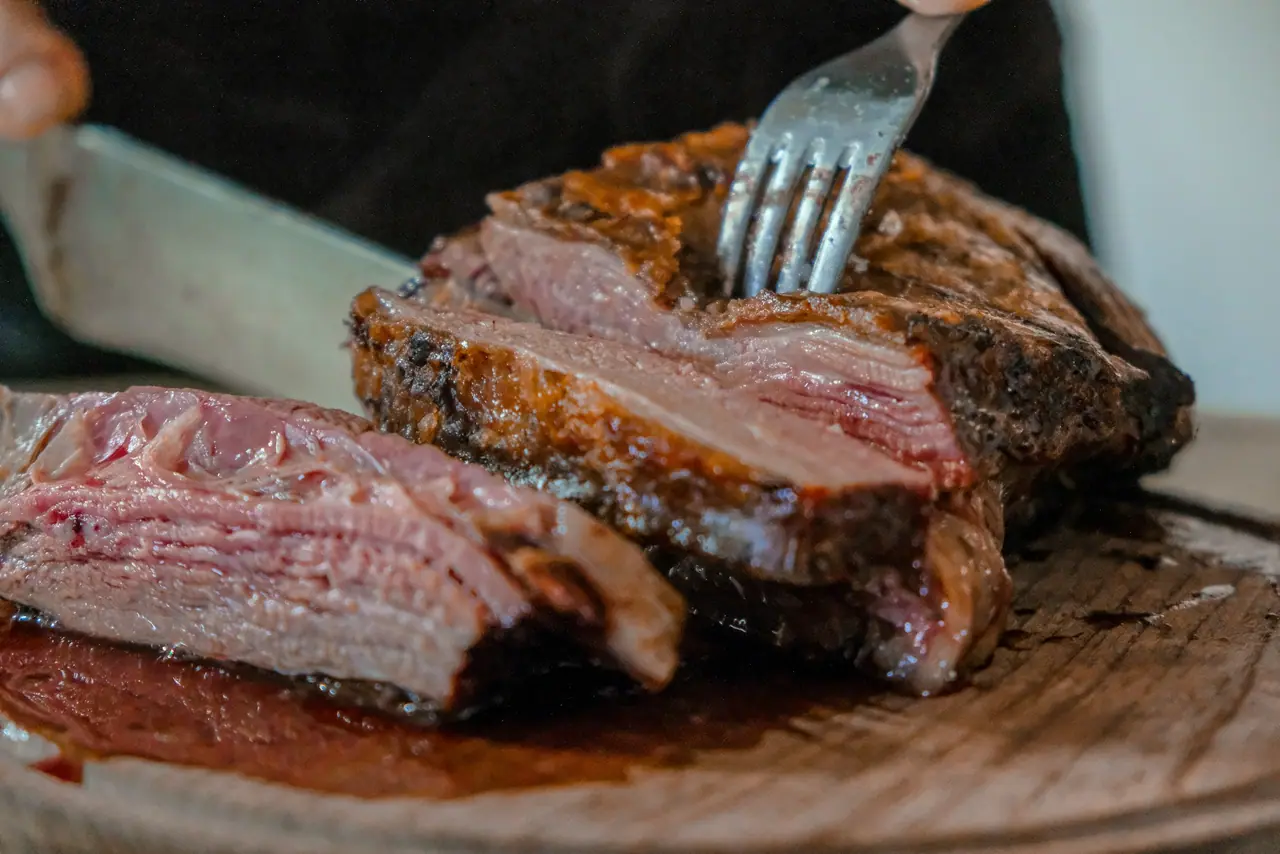 Corte de carne bovina fresca, com fibra e gordura aparentes, sendo trinchado com garfo