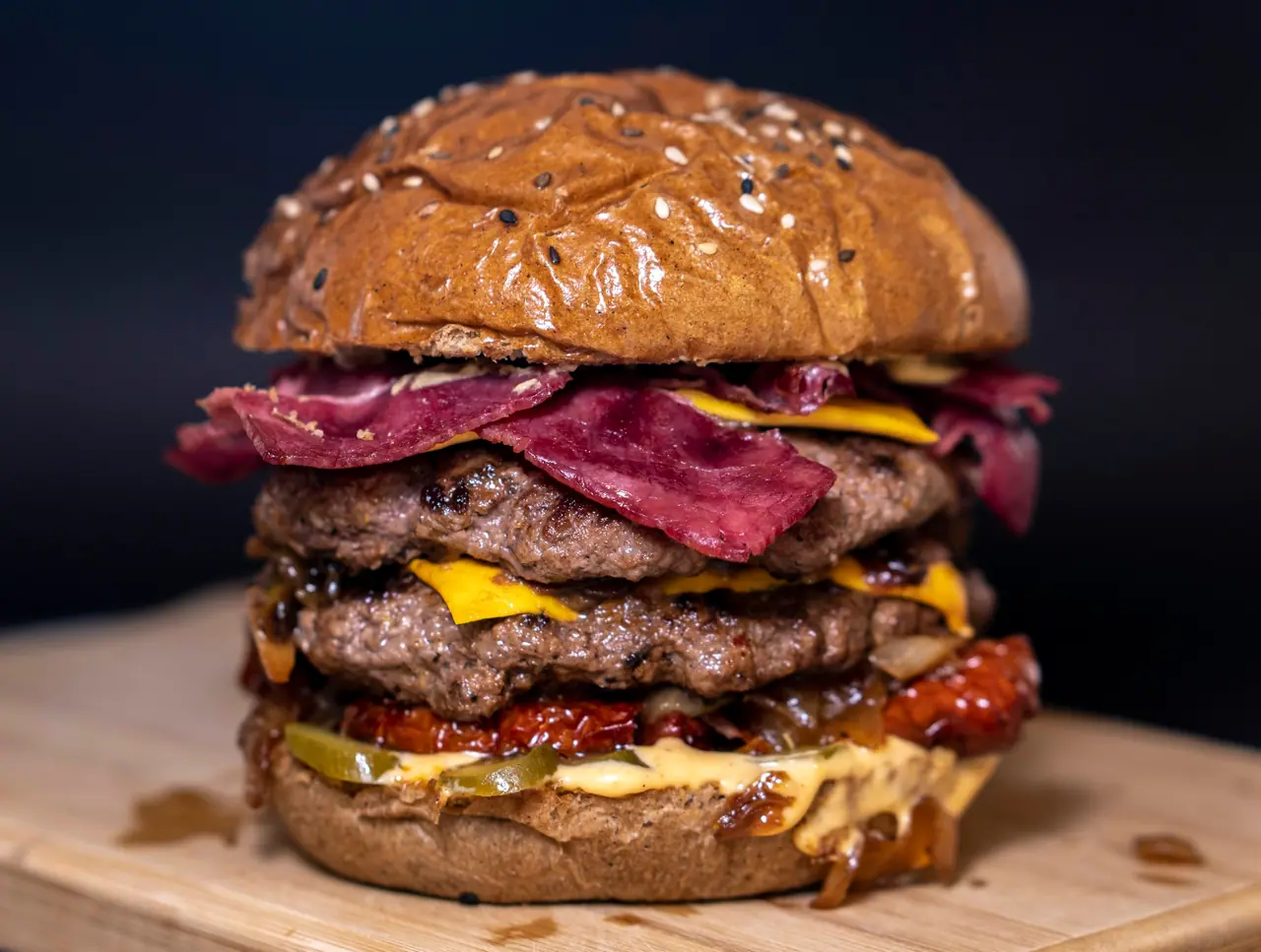 Hambúrguer alto com duas carnes, bacon e cheddar derretido, em close