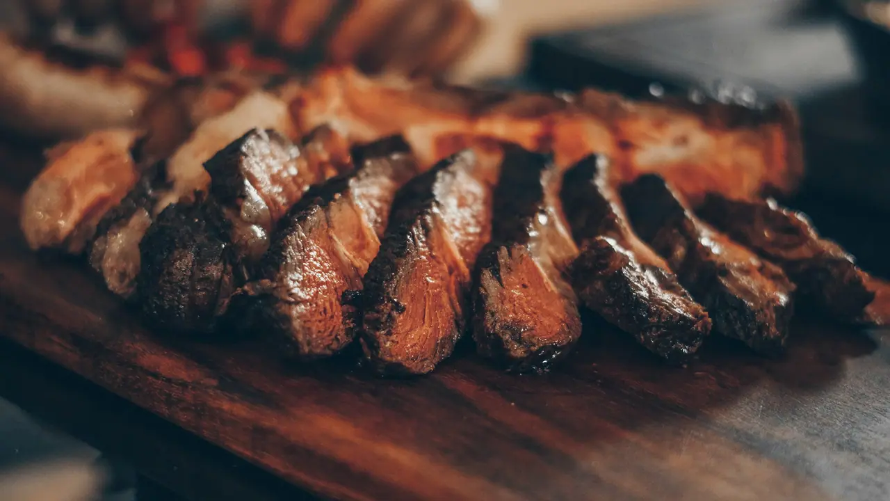 Carne grelhada na chapa e fatiada sobre tábua, com marcas de brasa
