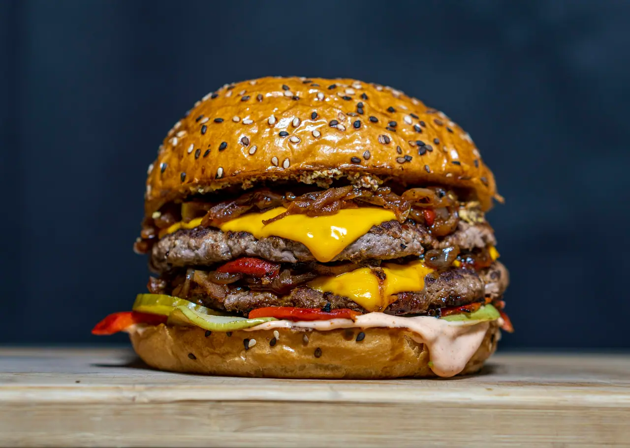 Hambúrguer Smash Duplo com duas carnes finas de bordas crocantes, queijo derretido e picles, em fundo azul escuro