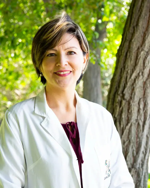 Dra. Helena Prado, fisioterapeuta, sorrindo, de jaleco, ao ar livre