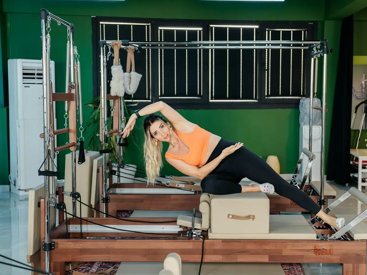 Mulher fazendo exercício de pilates em aparelho, em estúdio com paredes verdes
